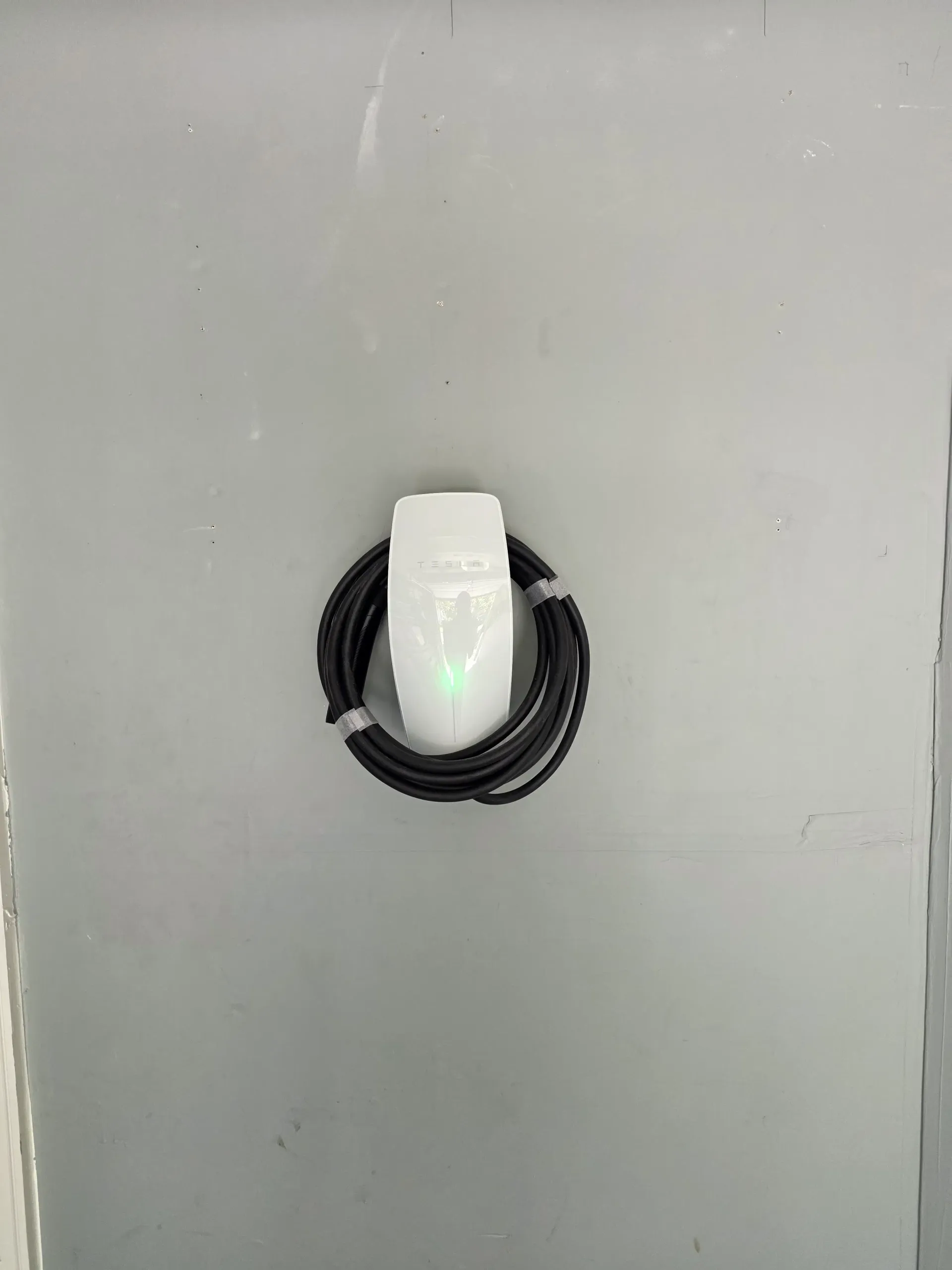 Tesla Wall Connector mounted on a gray wall in Ashburn, Virginia, with the charging cable coiled
