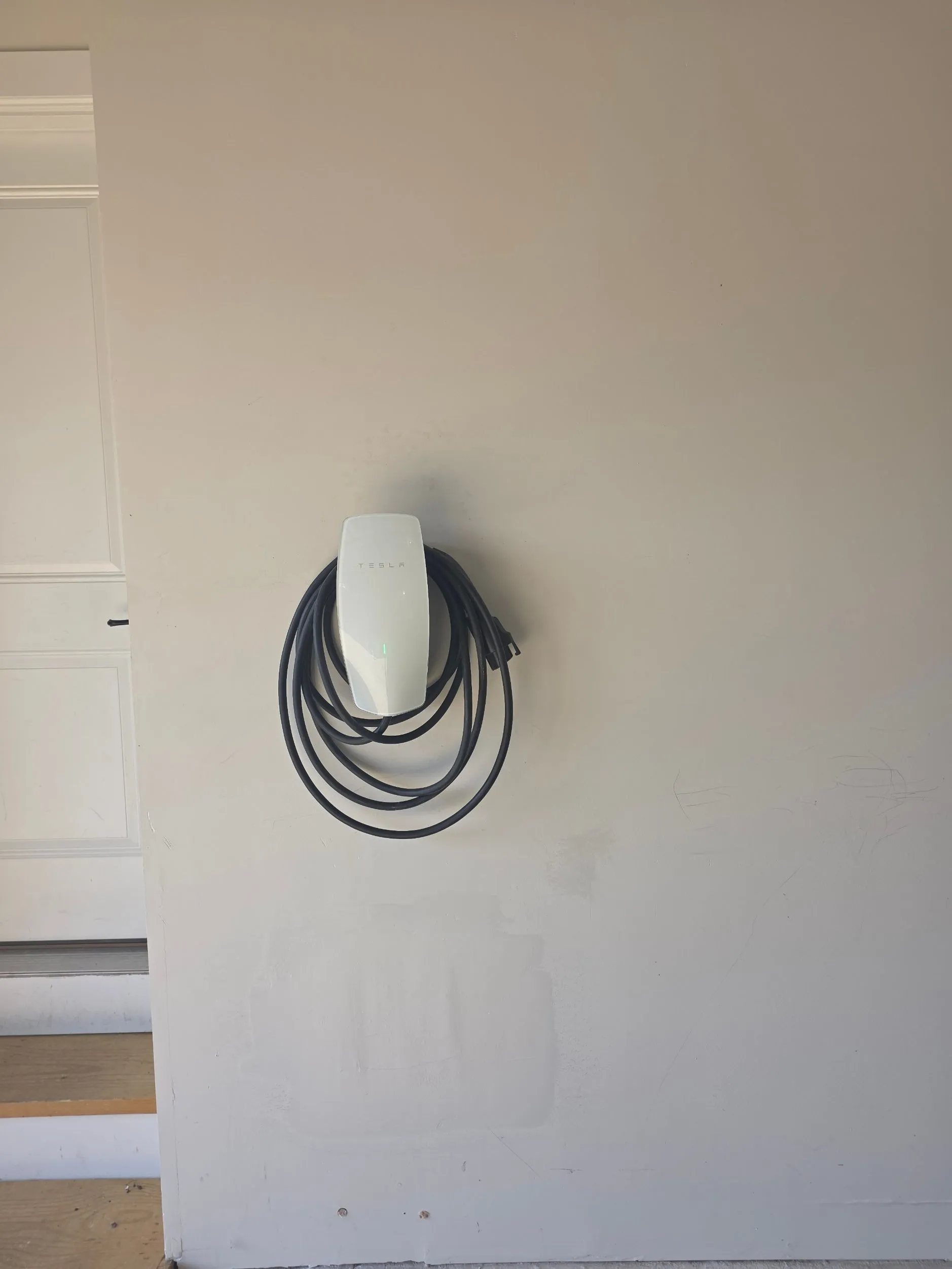 Tesla Wall Connector mounted on a residential wall with the charging cable coiled