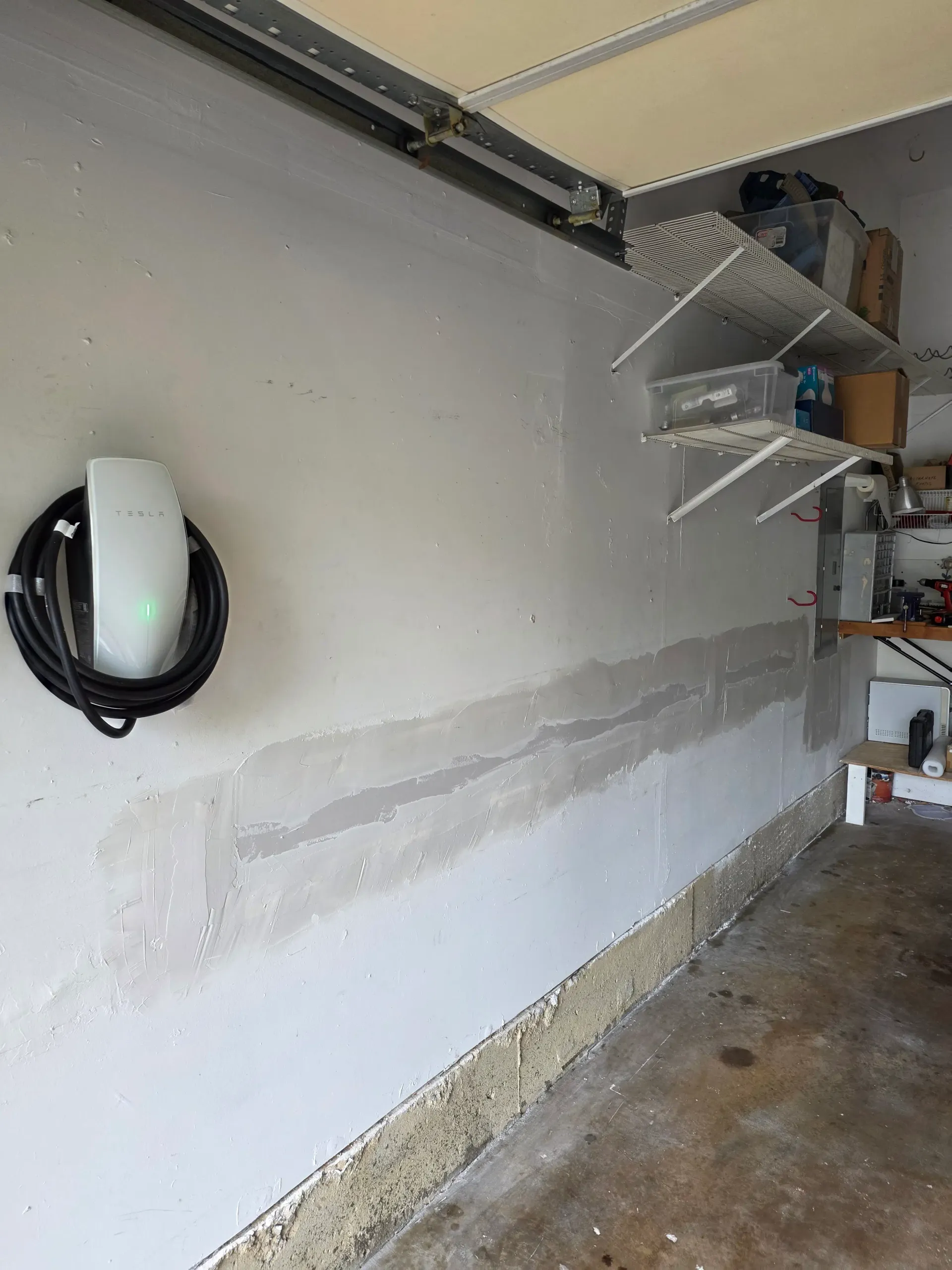 Tesla Wall Connector mounted on a garage wall in Broadlands, Virginia, with a visible drywall patch below