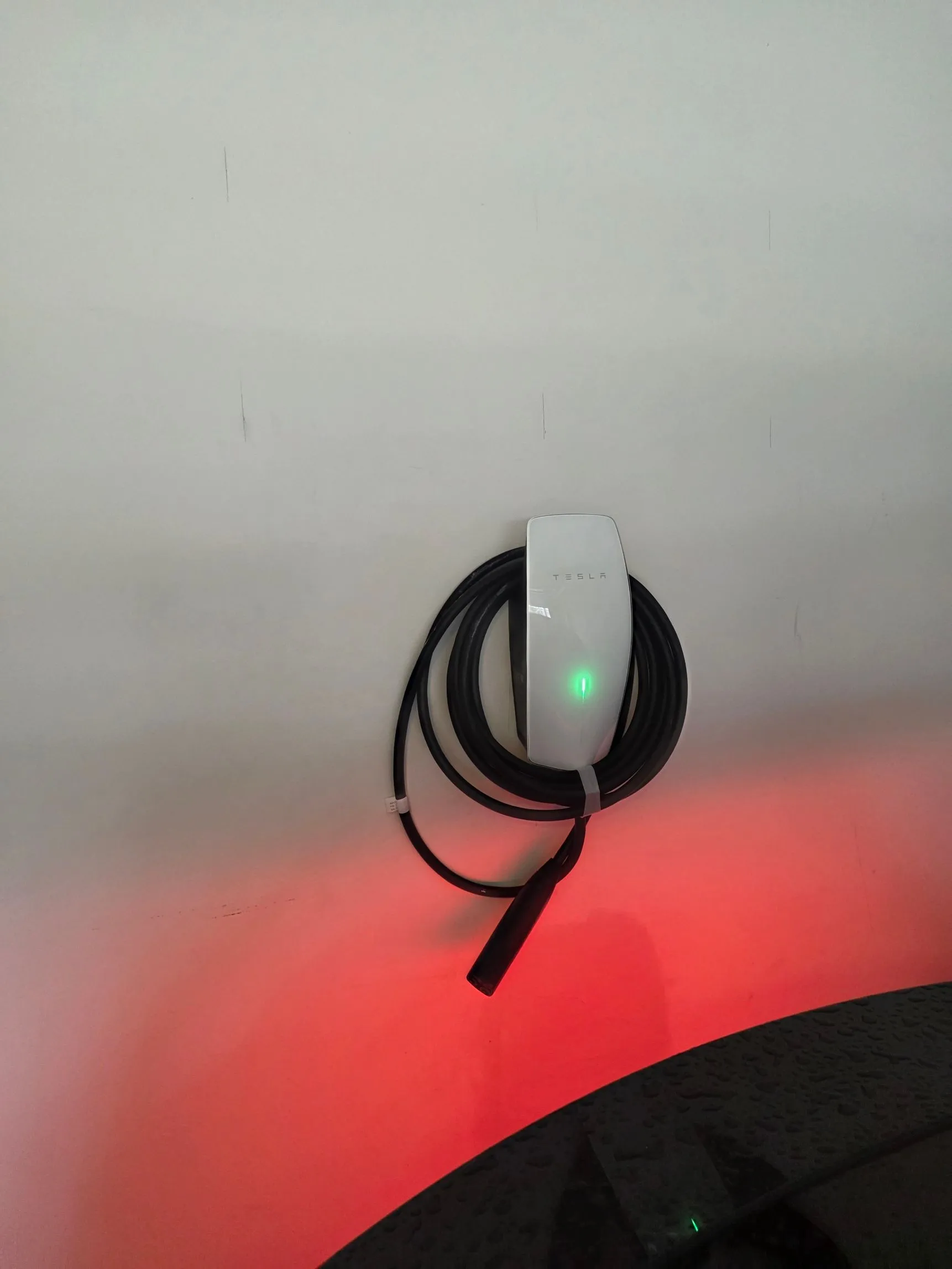 Tesla Wall Connector mounted on a wall in Chantilly, Virginia, powered on with its green status light and the charging cable neatly coiled
